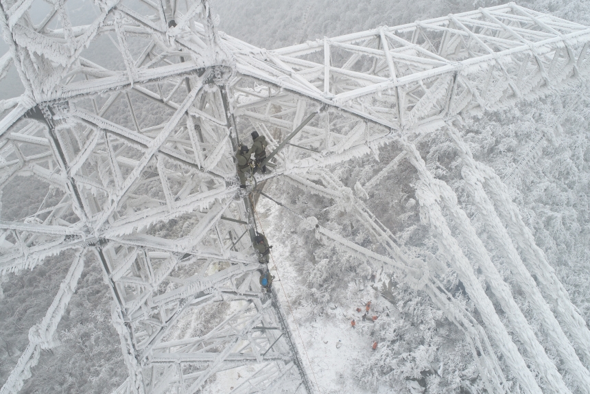 電力應(yīng)急處置人員爬上70米高的±800千伏陜武輸電線路1898號塔，通過機械震動方式清除地線和光纜上的積雪。鄒小民攝 