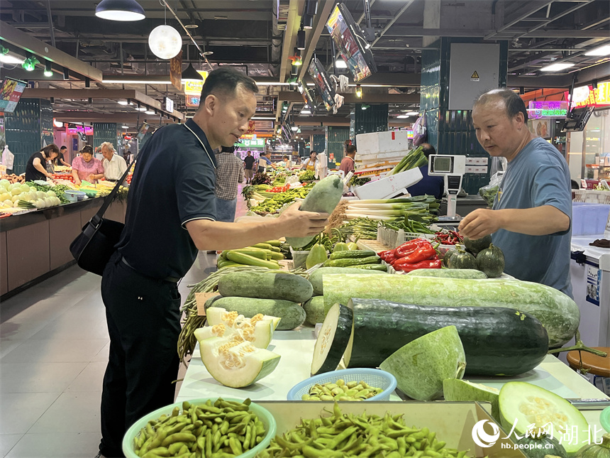 晚高峰時(shí)段，一名背著公文包的男士路過洪山廣場地鐵站菜市場買菜。人民網(wǎng)記者 張雋攝